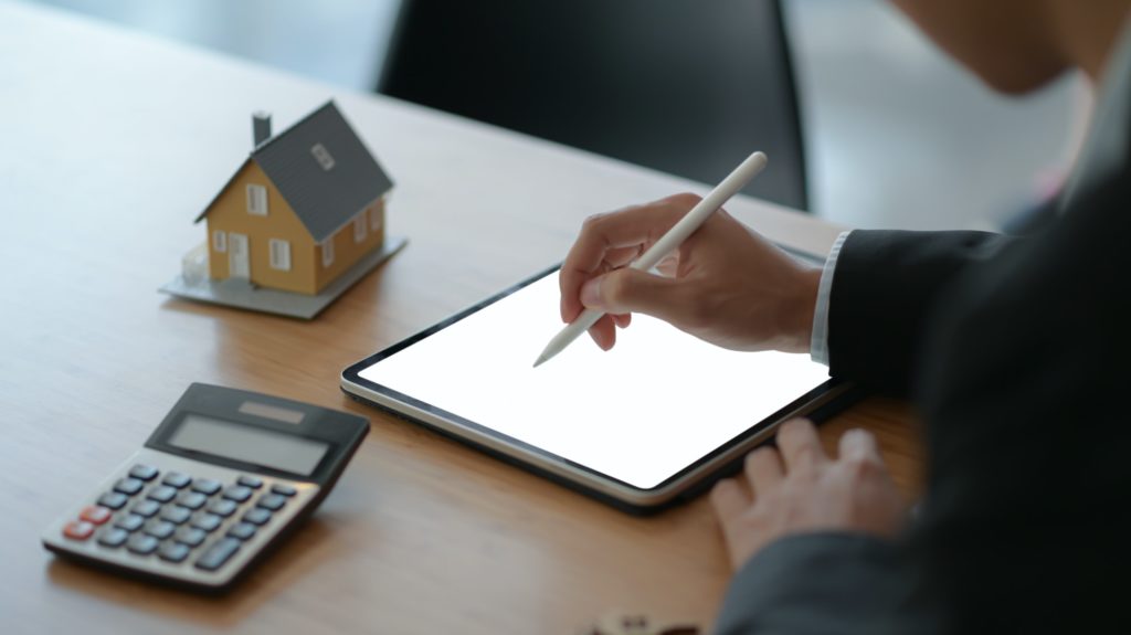 businesspeople use a pen to write on a tablet with model house and a calculator on the table